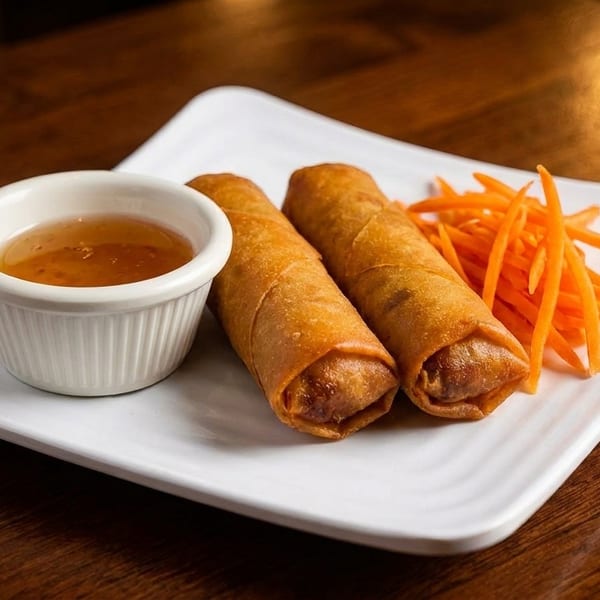 Two crispy spring rolls, a side of shredded carrots, and a small dish of dipping sauce.
