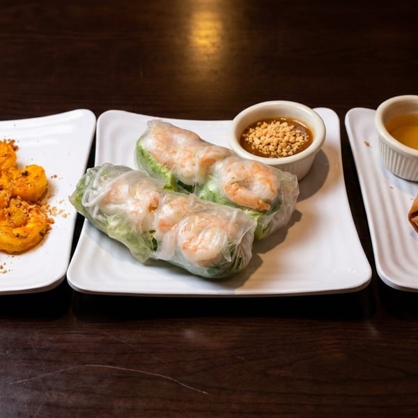 Three plates of Vietnamese appetizers: grilled shrimp, fresh spring rolls with peanut sauce, and fried egg rolls.
