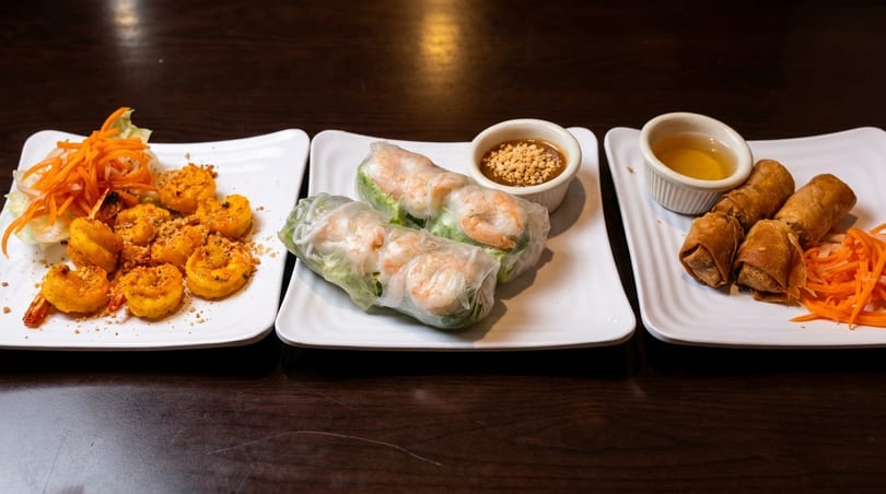 Three plates of Vietnamese appetizers: grilled shrimp, fresh spring rolls with peanut sauce, and fried egg rolls.