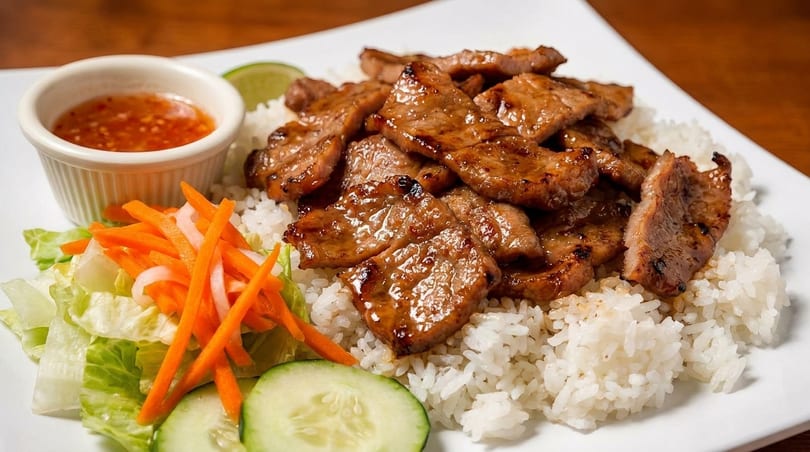 Grilled pork slices over white rice, with a side salad, cucumber, and dipping sauce.