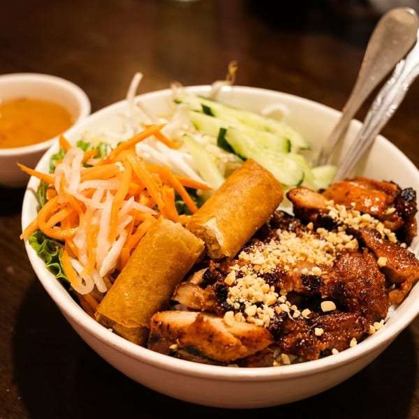 A Vietnamese vermicelli bowl with grilled chicken, spring rolls, and fresh vegetables.