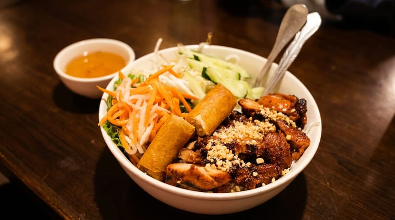 A Vietnamese vermicelli bowl with grilled chicken, spring rolls, and fresh vegetables.